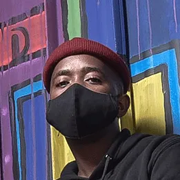 A young man in a red beanie and black face mask in front of a colourful mural